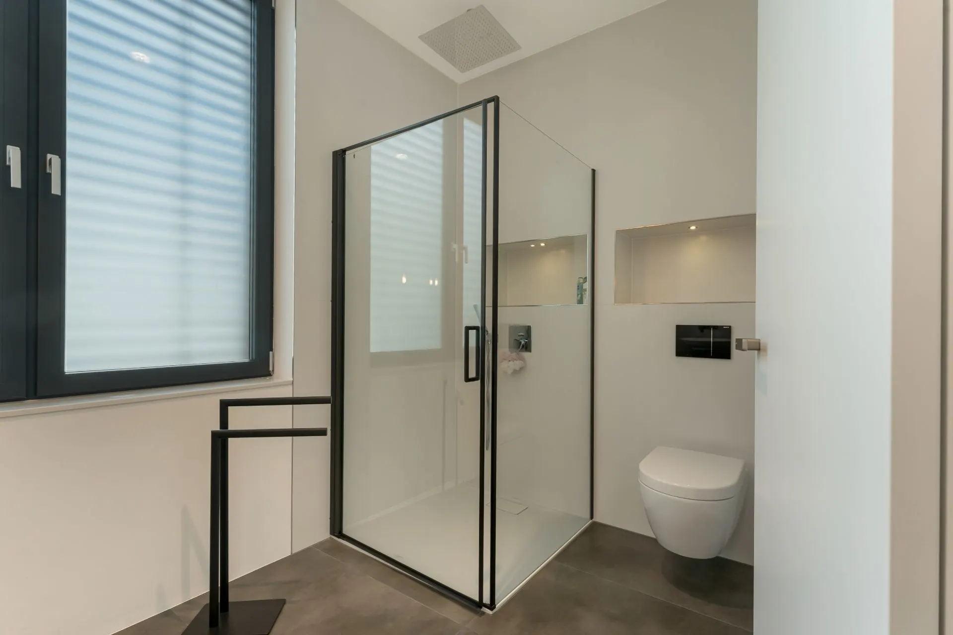 Modernes Bad mit Glasdusche, wandhängender Toilette und Fenster mit Jalousie.