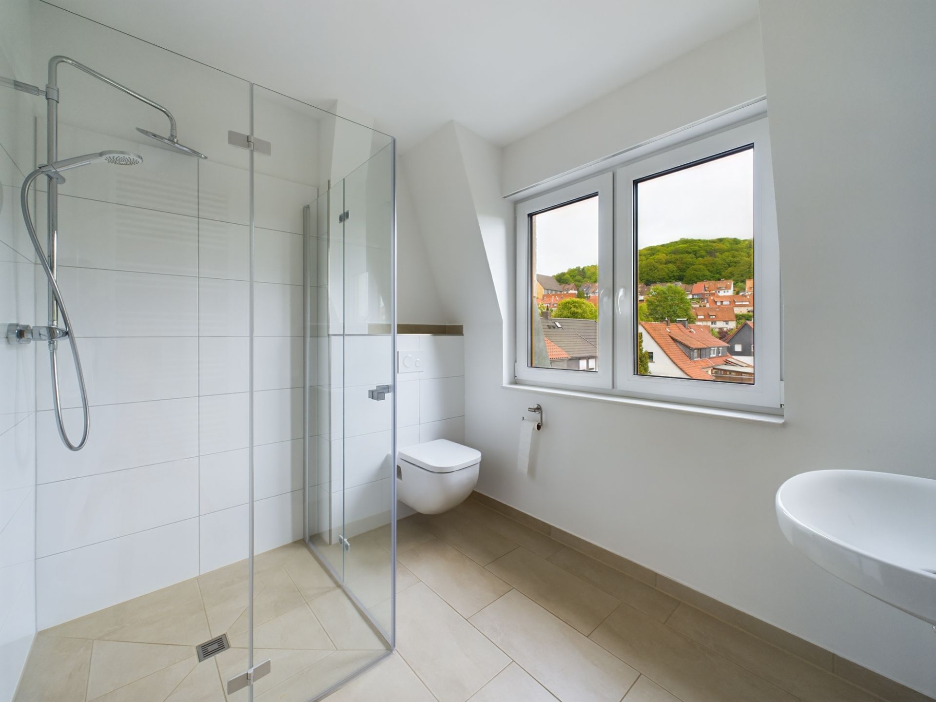 Modernes Badezimmer mit bodengleicher Dusche, WC, Waschbecken und großem Fenster.
