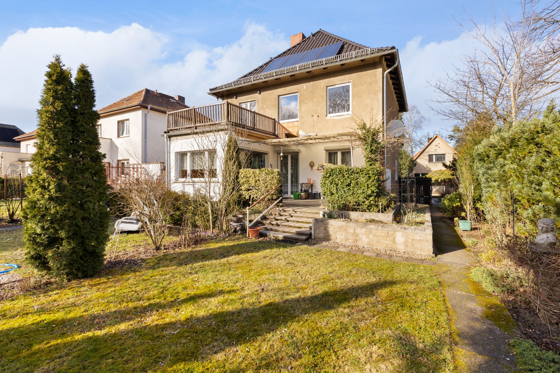 Zweistöckiges Wohnhaus mit Terrasse, Treppe und Garten im Vordergrund.