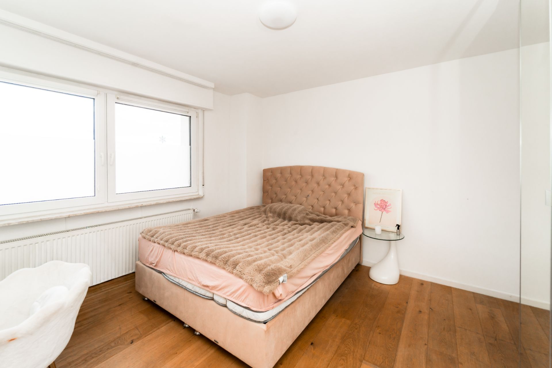 Helles Schlafzimmer mit Bett, Nachttisch und großem Fenster auf Holzfußboden.