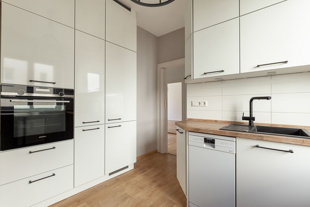 Moderne Küche mit weißen Schränken, Einbauofen, Spülmaschine und Spüle.