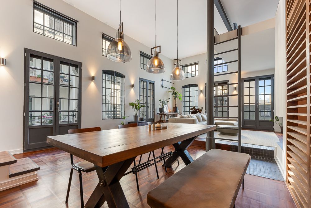 Helles Wohnzimmer mit Holztisch, modernen Lampen, Sofa und vielen Fenstern mit schwarzen Rahmen.