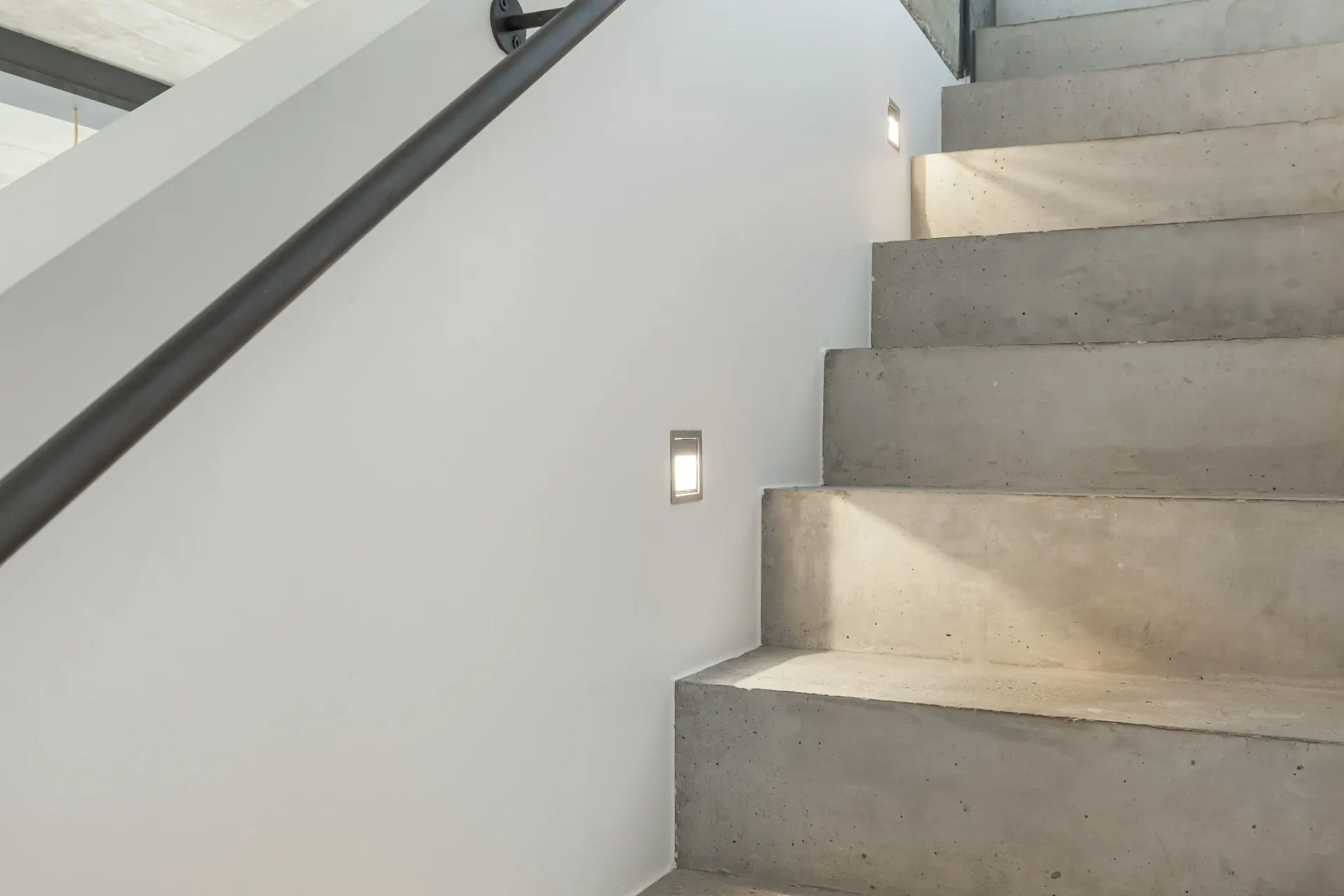Betontreppe mit Wandgeländer und eingelassenen Stufenleuchten in einem modernen Wohnhaus.