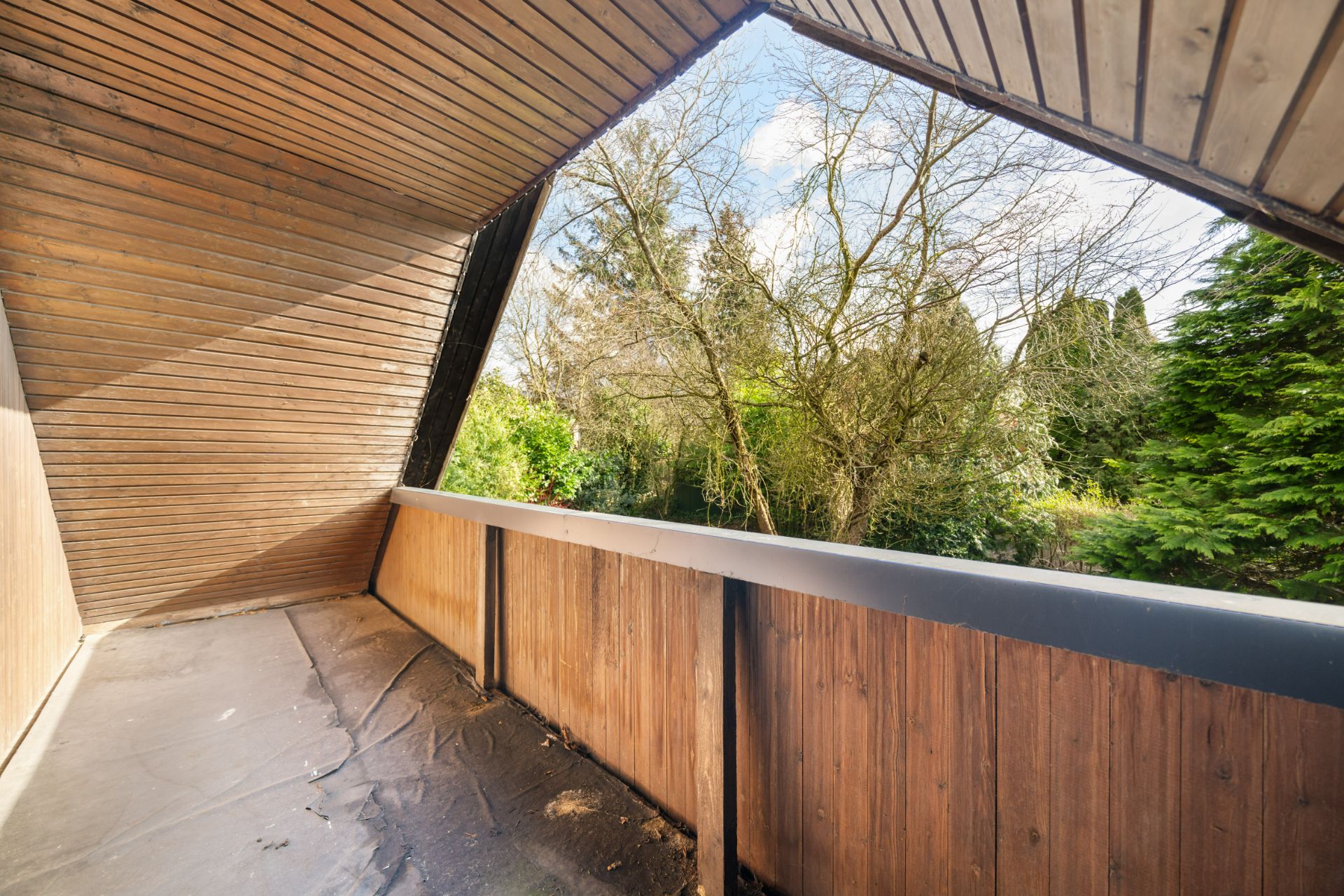 Überdachter Balkon mit Holzverkleidung und Blick auf Bäume im Garten.
