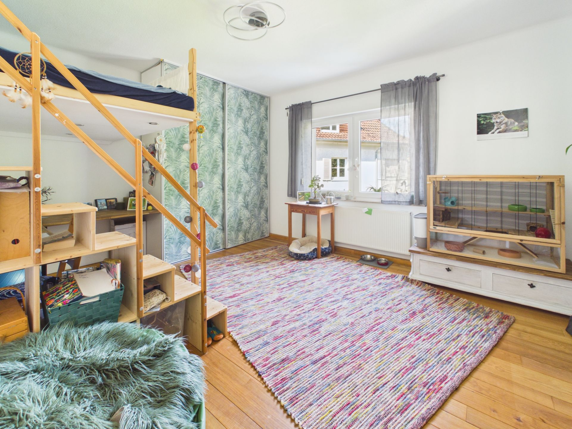 Helles Kinderzimmer mit Hochbett, Teppich, Schrank, Fenster und großem Kleintierkäfig.
