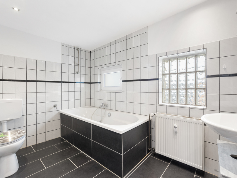 Modernes Badezimmer mit Badewanne, Toilette, Waschbecken und Fenster mit Glasbausteinen.