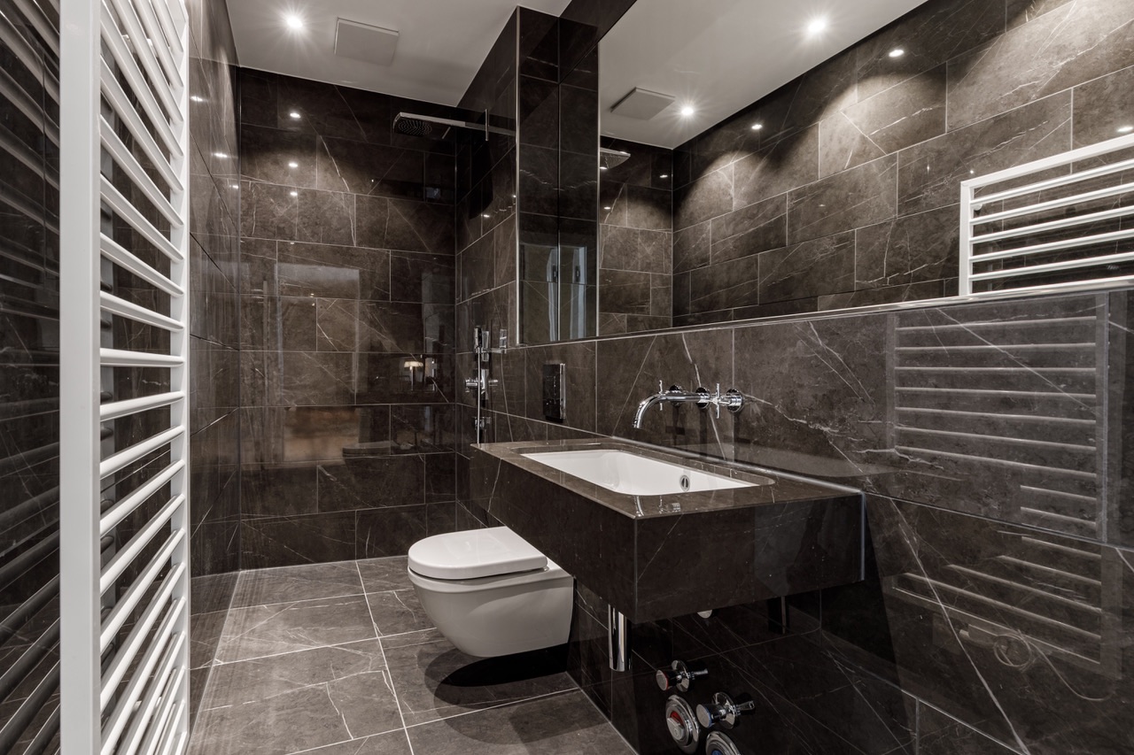 Modernes Badezimmer mit dunklen Fliesen, Wandwaschbecken, Toilette und Handtuchheizkörper.