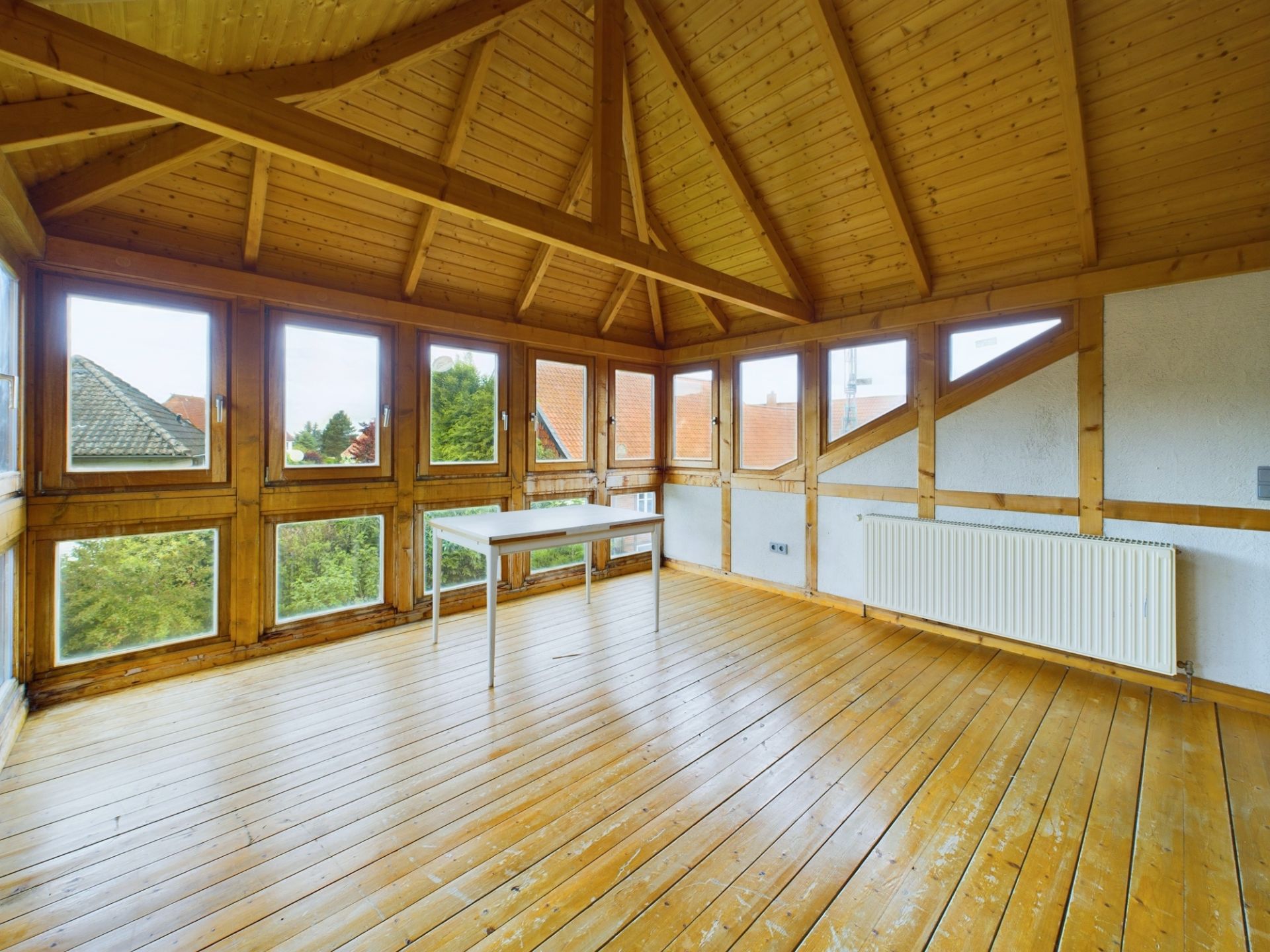 Heller Raum mit Holzdecke, großen Fenstern und einem einfachen weißen Tisch.