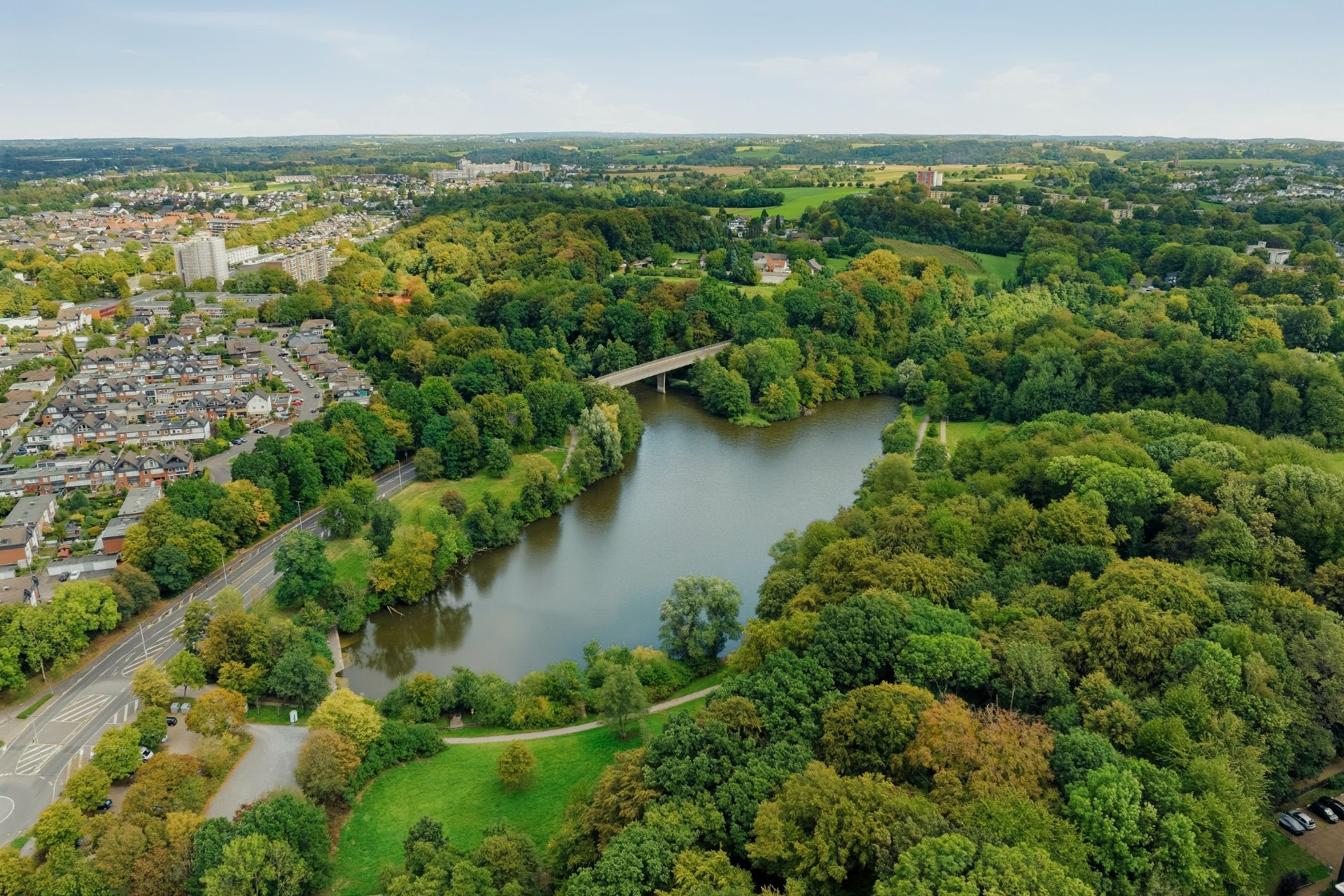 Luftaufnahme eines Parks mit See, Brücke und umliegenden Wohnhäusern.