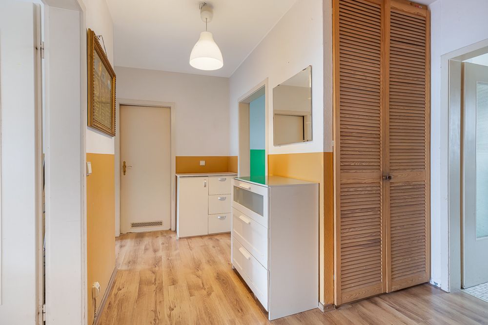 Flur mit Holzfußboden, weißen Möbeln, Spiegel und Holzschrank mit Lamellentüren.