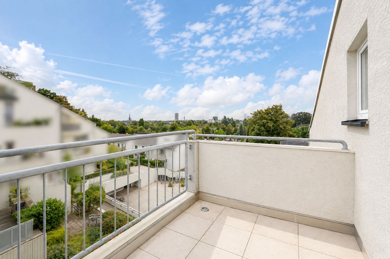 Heller Balkon mit Fliesenboden und Metallgeländer, Blick auf grüne Umgebung und den Himmel.