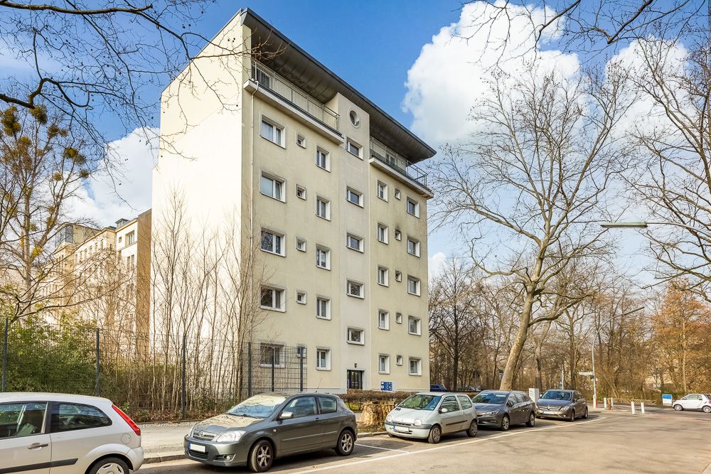 Mehrstöckiges Wohngebäude mit mehreren Fenstern, davor parken Autos an der Straße.