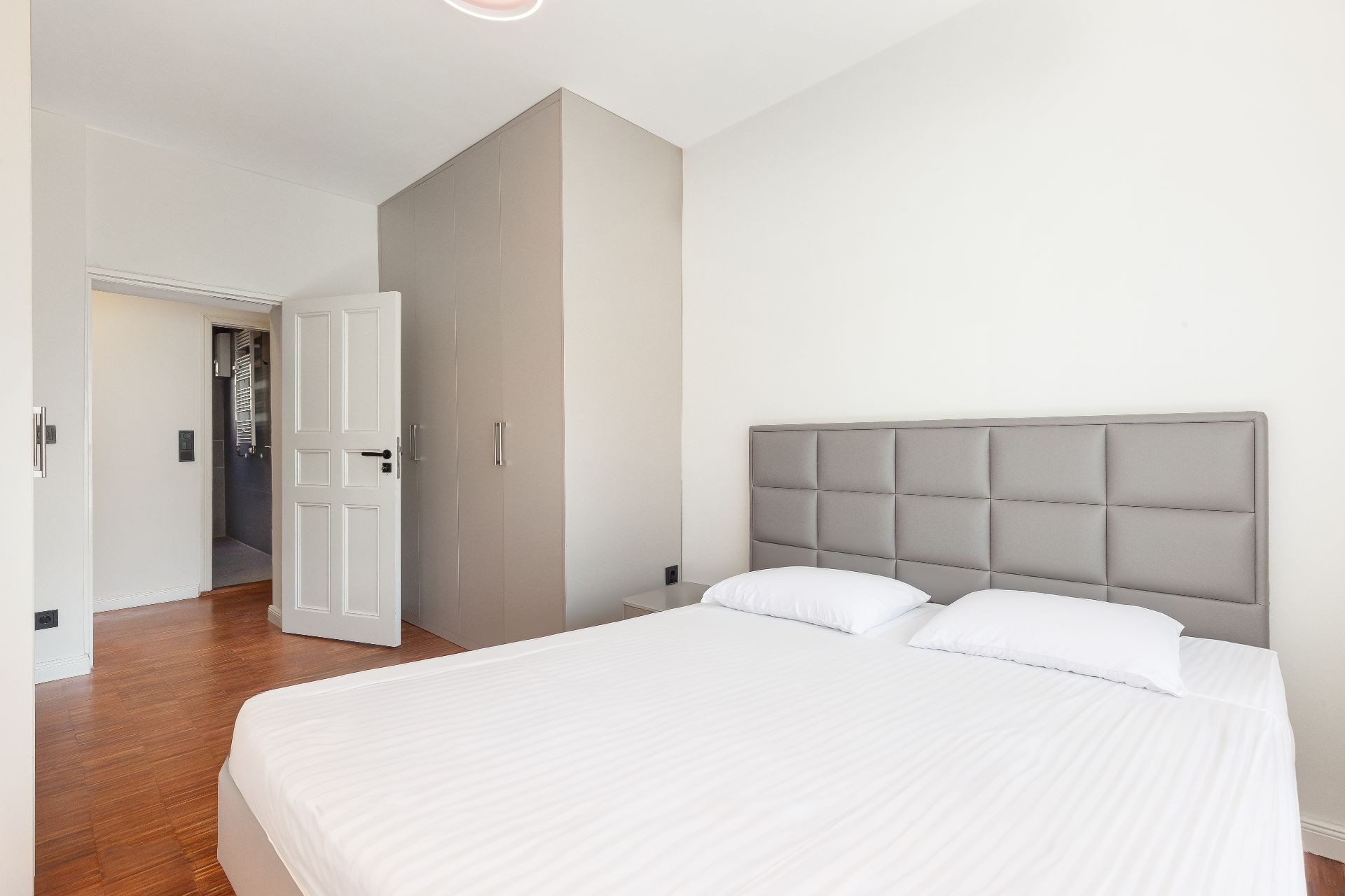 Helles Schlafzimmer mit Doppelbett, grauem Kopfteil und großem Kleiderschrank.