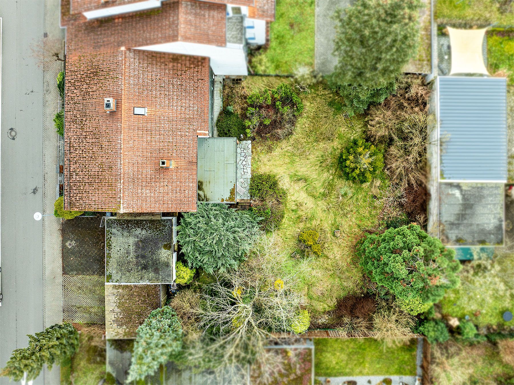 Luftaufnahme eines Wohnhauses mit Garten und Auffahrt, umgeben von Bäumen und Nachbarhäusern.