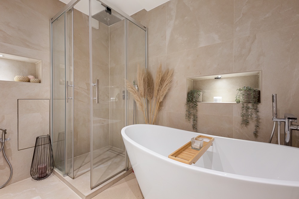 Modernes Badezimmer mit freistehender Badewanne, Glasdusche und Dekopflanzen an der Wand.