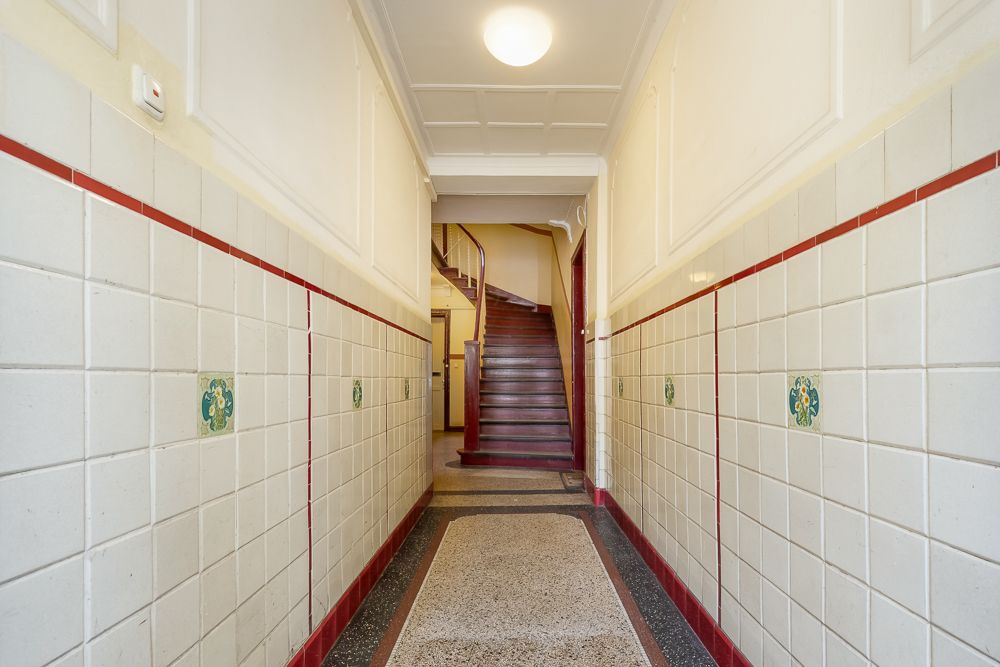 Heller Flur mit weißen Wandfliesen und einer Holztreppe am Ende.