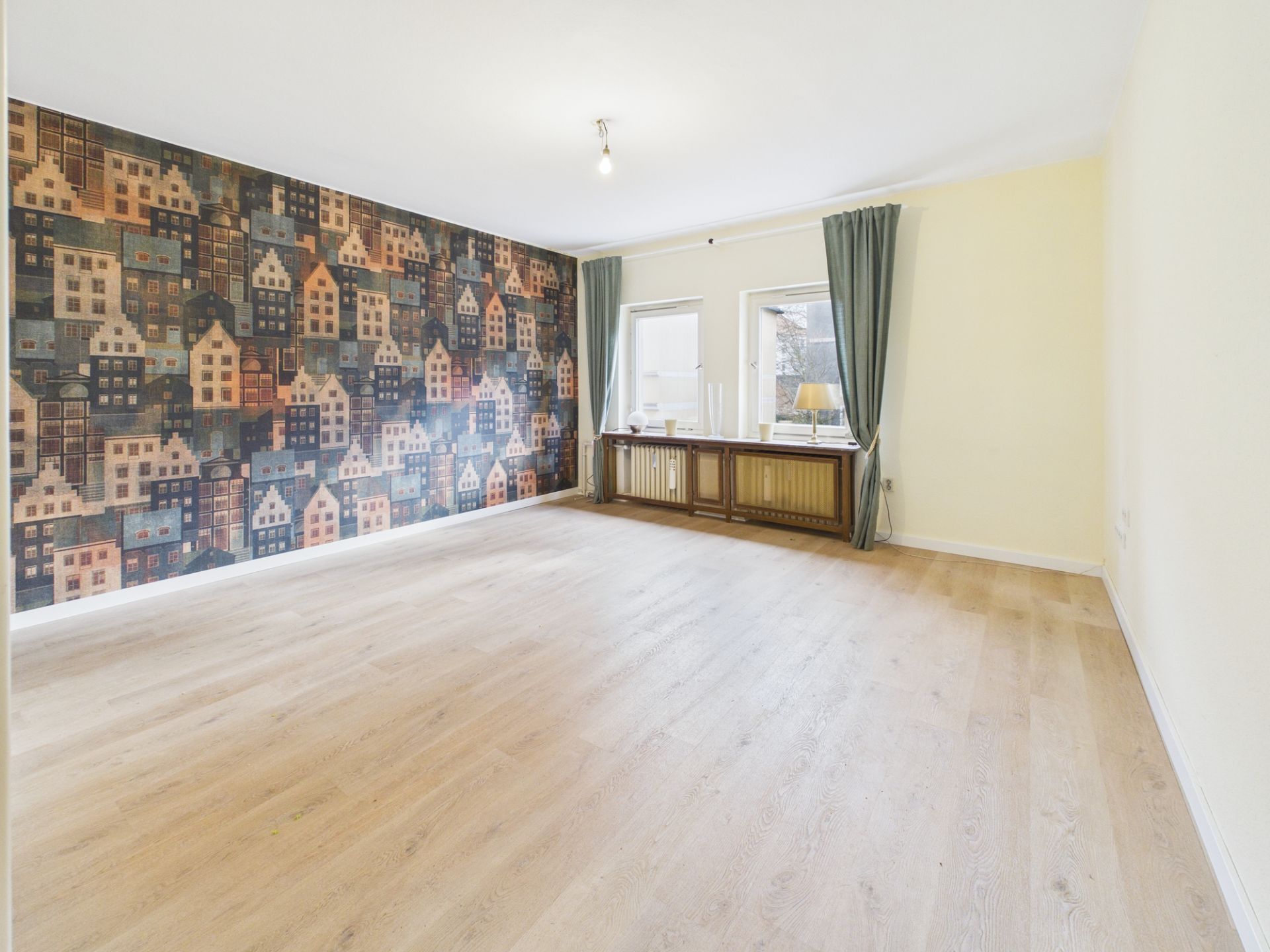 Helles Wohnzimmer mit Holzfußboden, Fenster, Vorhängen und bunter Tapete mit Häusern.