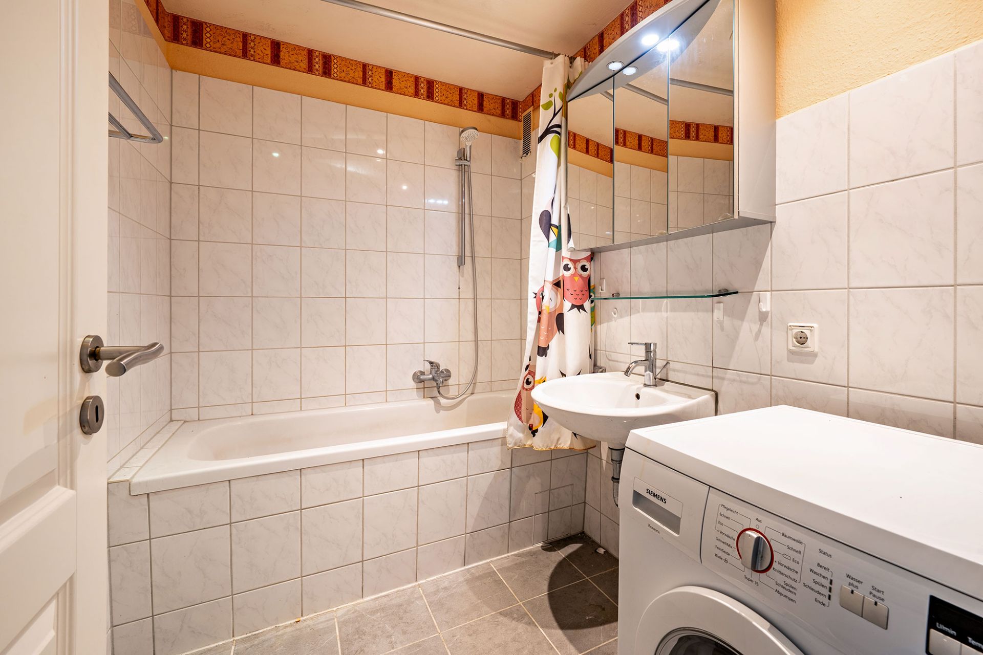 Badezimmer mit Badewanne, Waschbecken, Waschmaschine und Spiegelschrank.