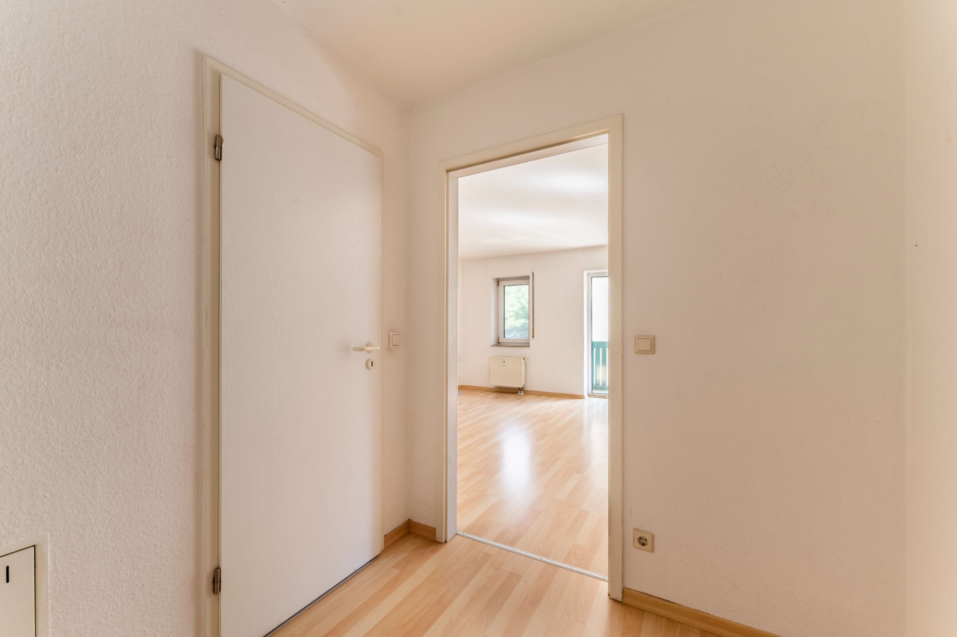 Heller Flur mit Holzboden und Blick in ein Zimmer mit zwei Fenstern.