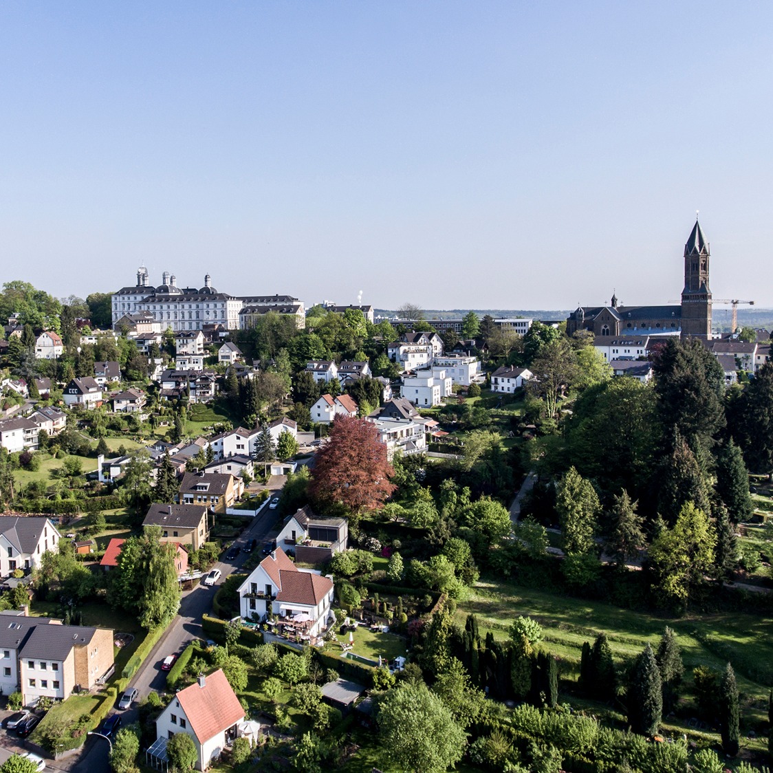 Luftaufnahme eines Wohngebiets mit vielen Häusern, viel Grün und einer großen Kirche.