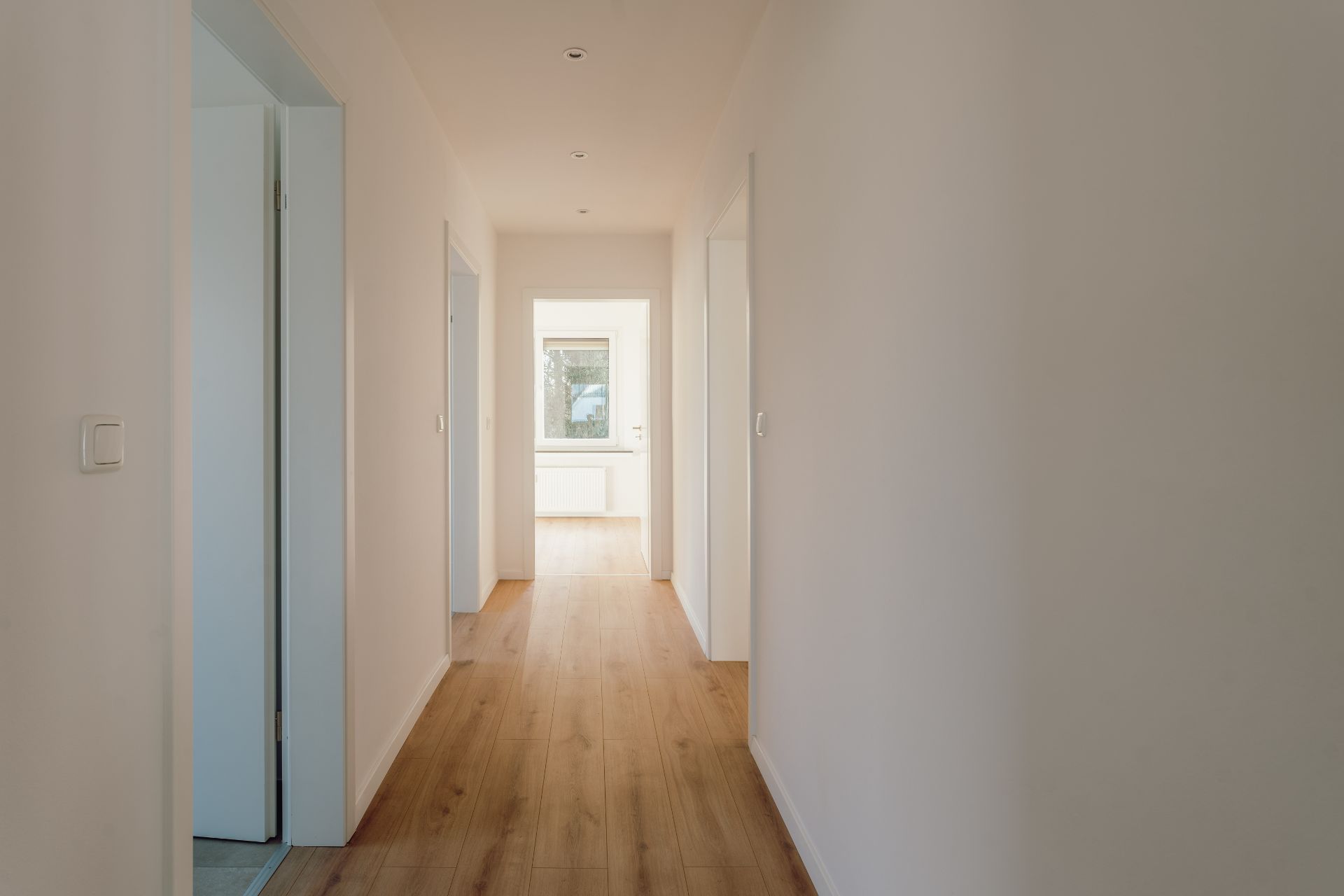 Heller Flur mit Holzboden, weißen Wänden und mehreren Türen in einem Wohnhaus.