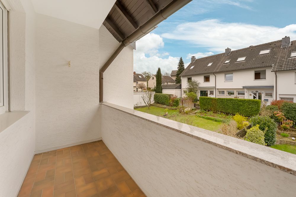 Überdachter Balkon mit braunen Fliesen, Blick auf Nachbargärten und Wohnhäuser.