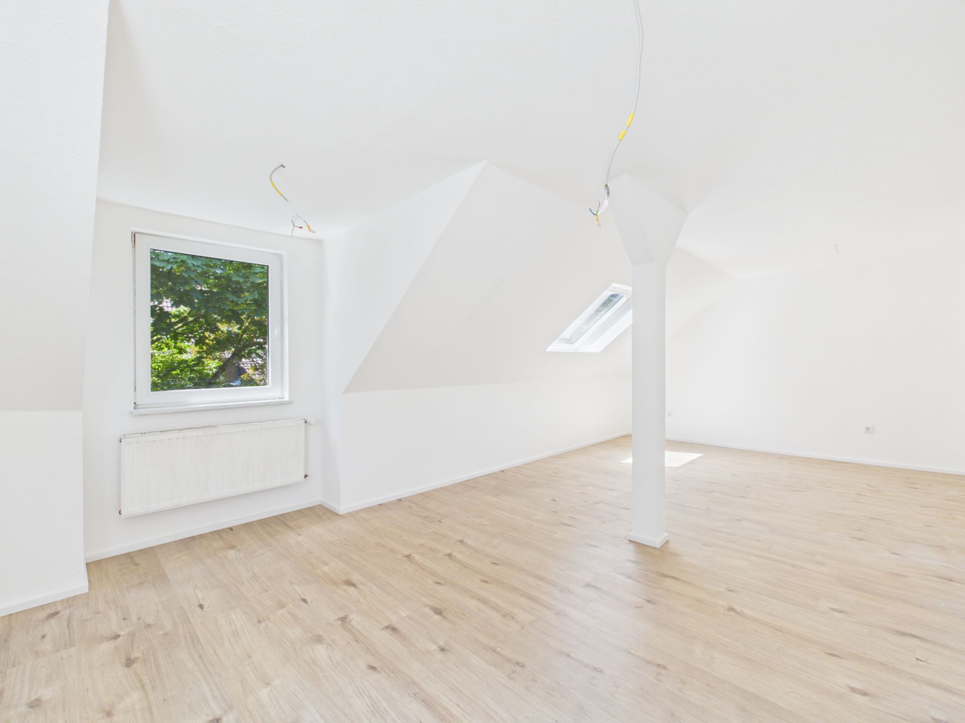 Helles Dachgeschosszimmer mit Holzfußboden, einem Fenster und einer weißen Stützsäule.