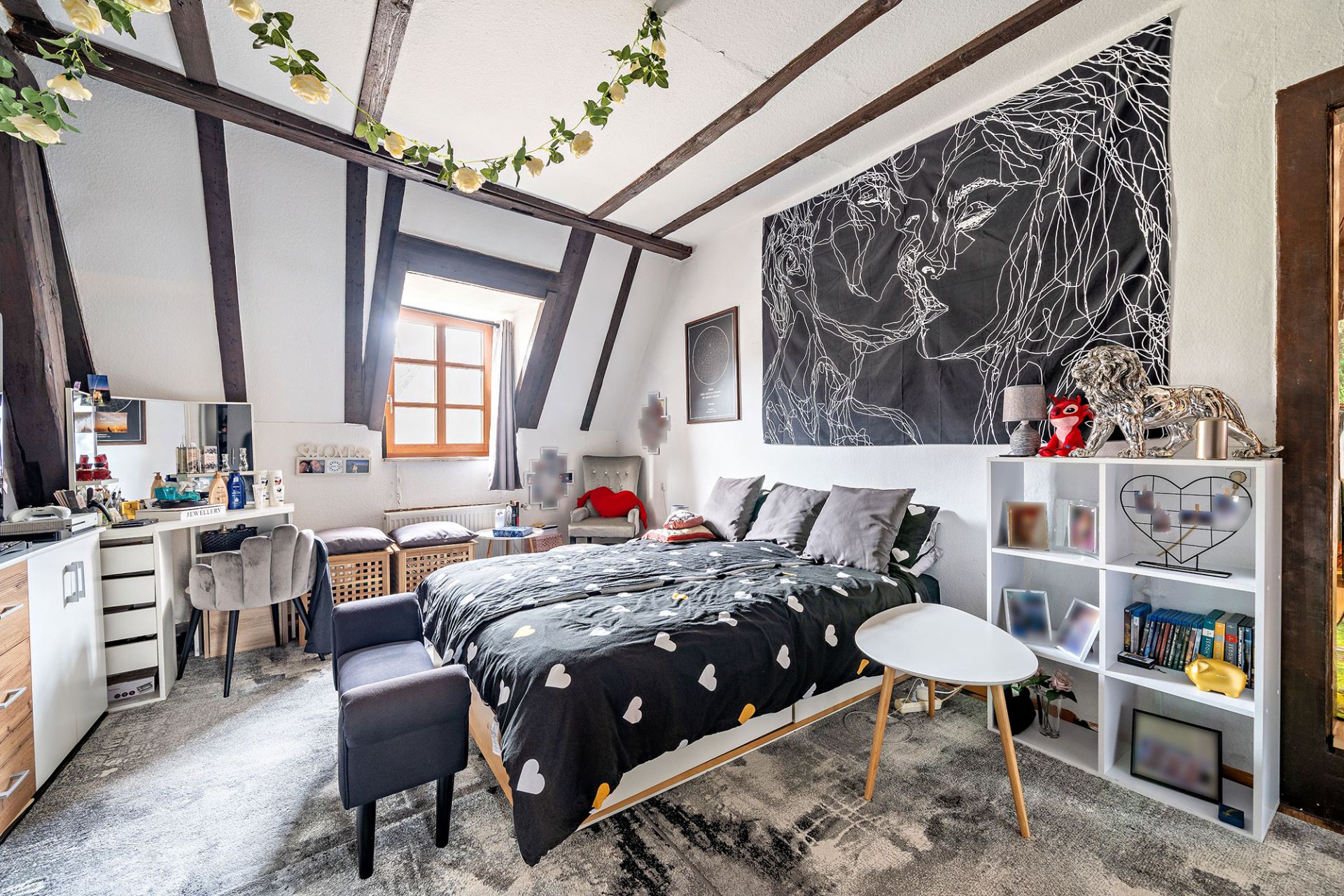 Helles Schlafzimmer mit Doppelbett, Schreibtisch, Regal und schrägen Holzbalken an der Decke.