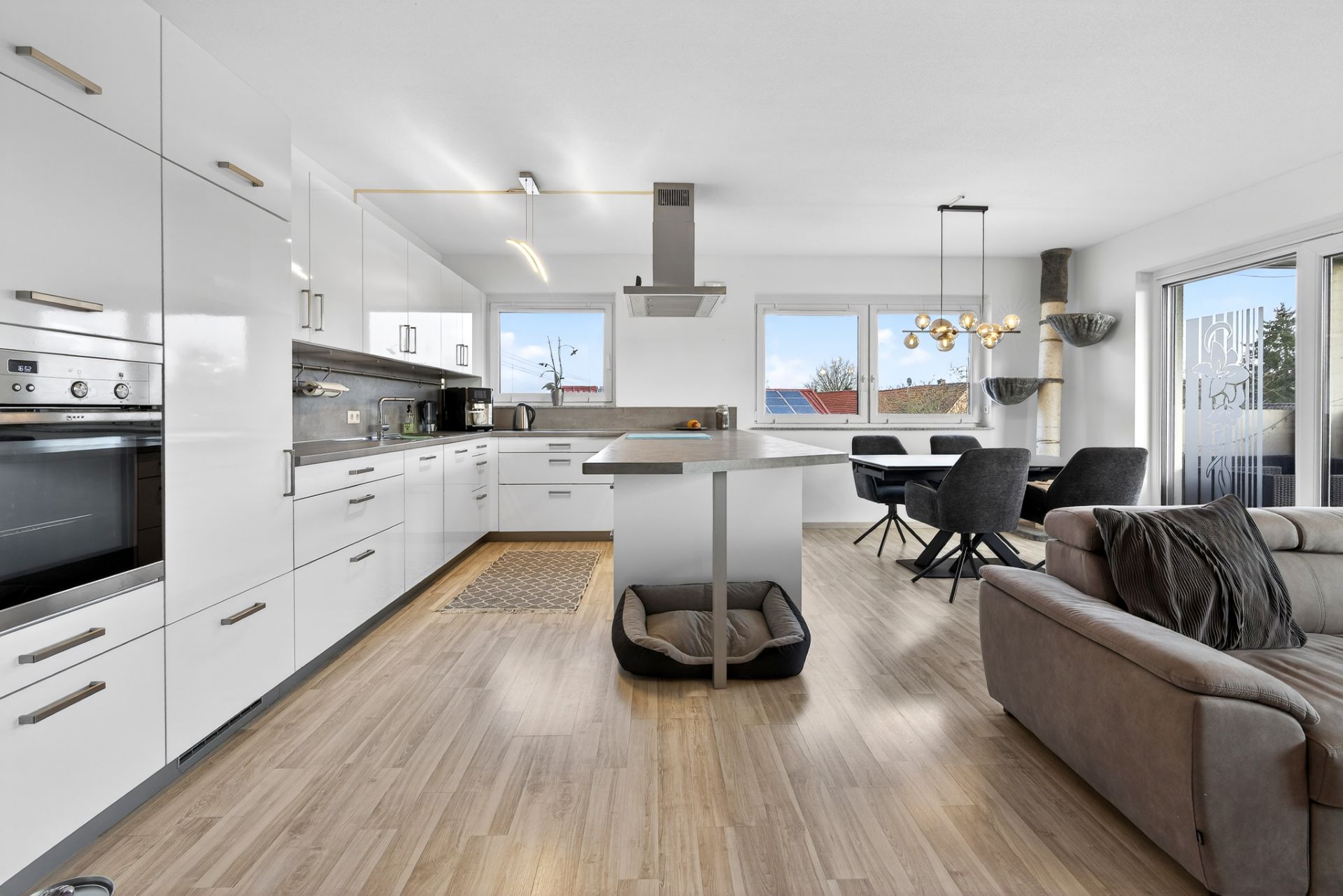 Moderne offene Küche mit Kochinsel, Essbereich und Sofa, Hundebett unter der Insel.