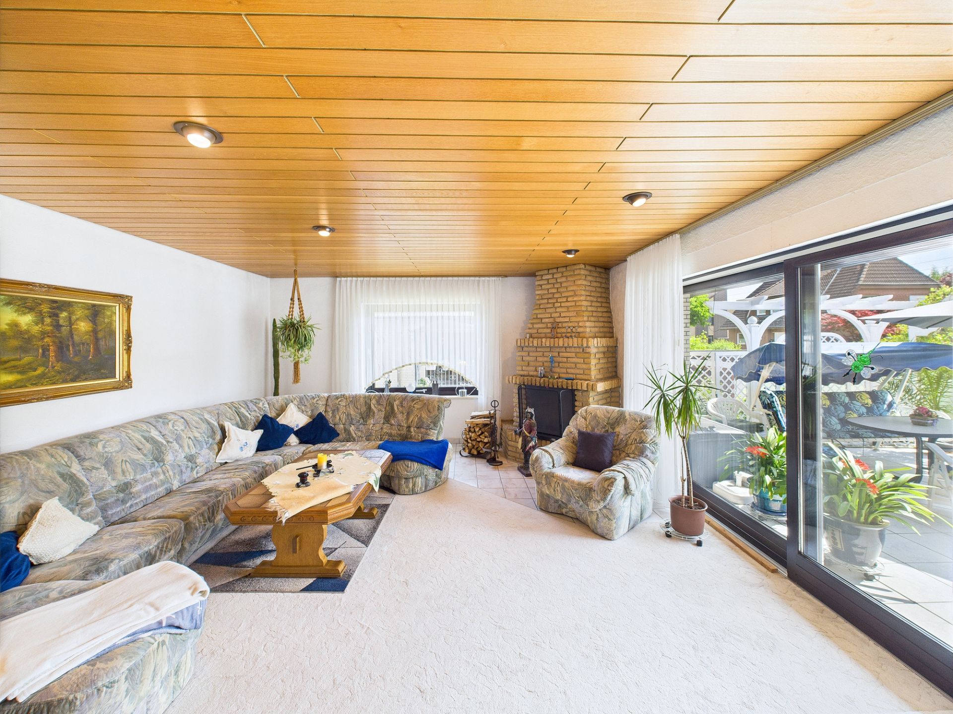 Helles Wohnzimmer mit Ecksofa, Sessel, Kamin und großen Fenstern zum Garten.