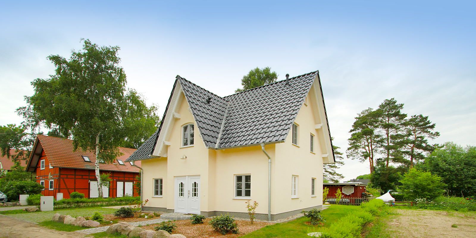 Freistehendes, helles Einfamilienhaus mit Satteldach und Garten, umgeben von Bäumen.