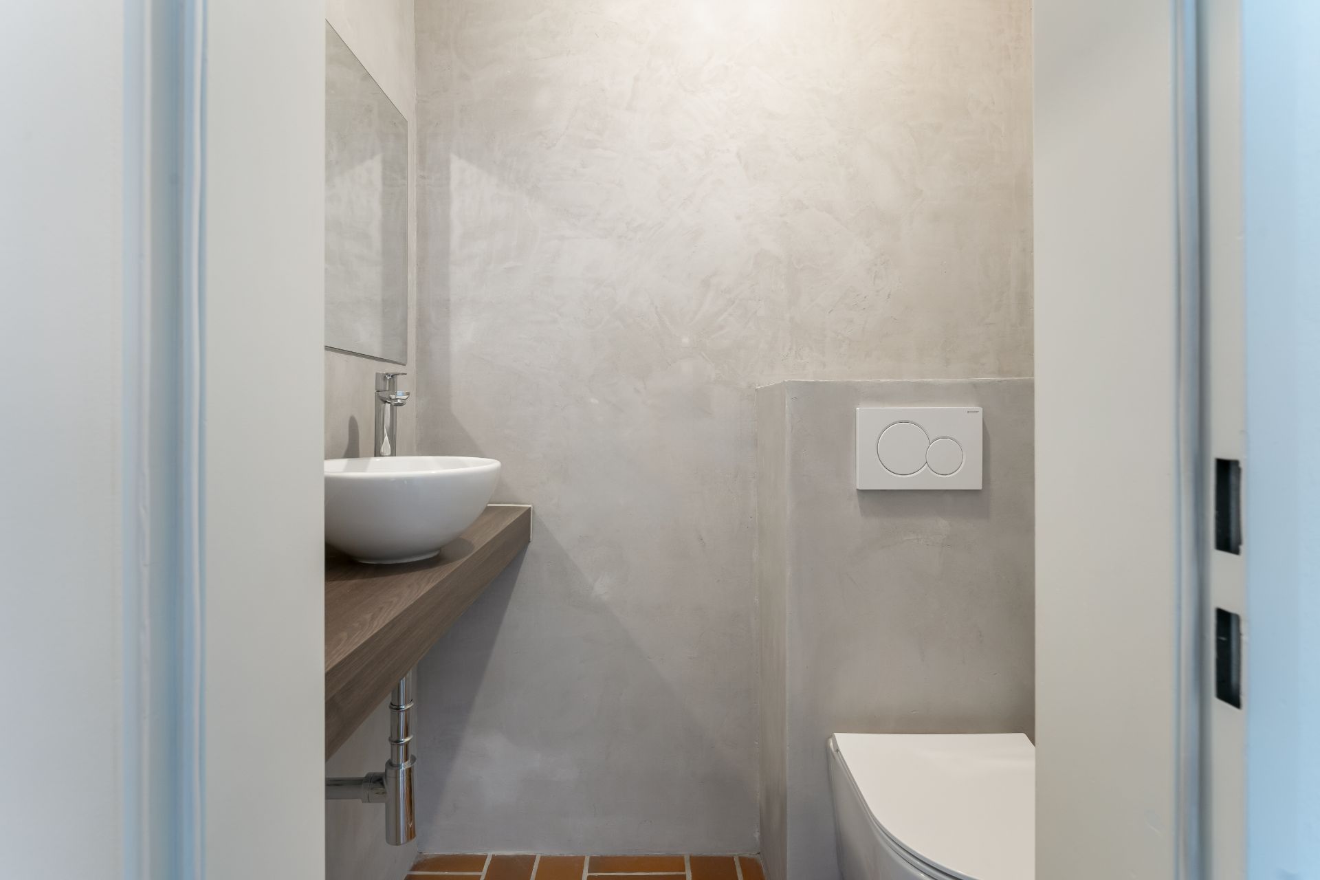 Kleines Badezimmer mit moderner Toilette und rundem Waschbecken auf Holzablage.