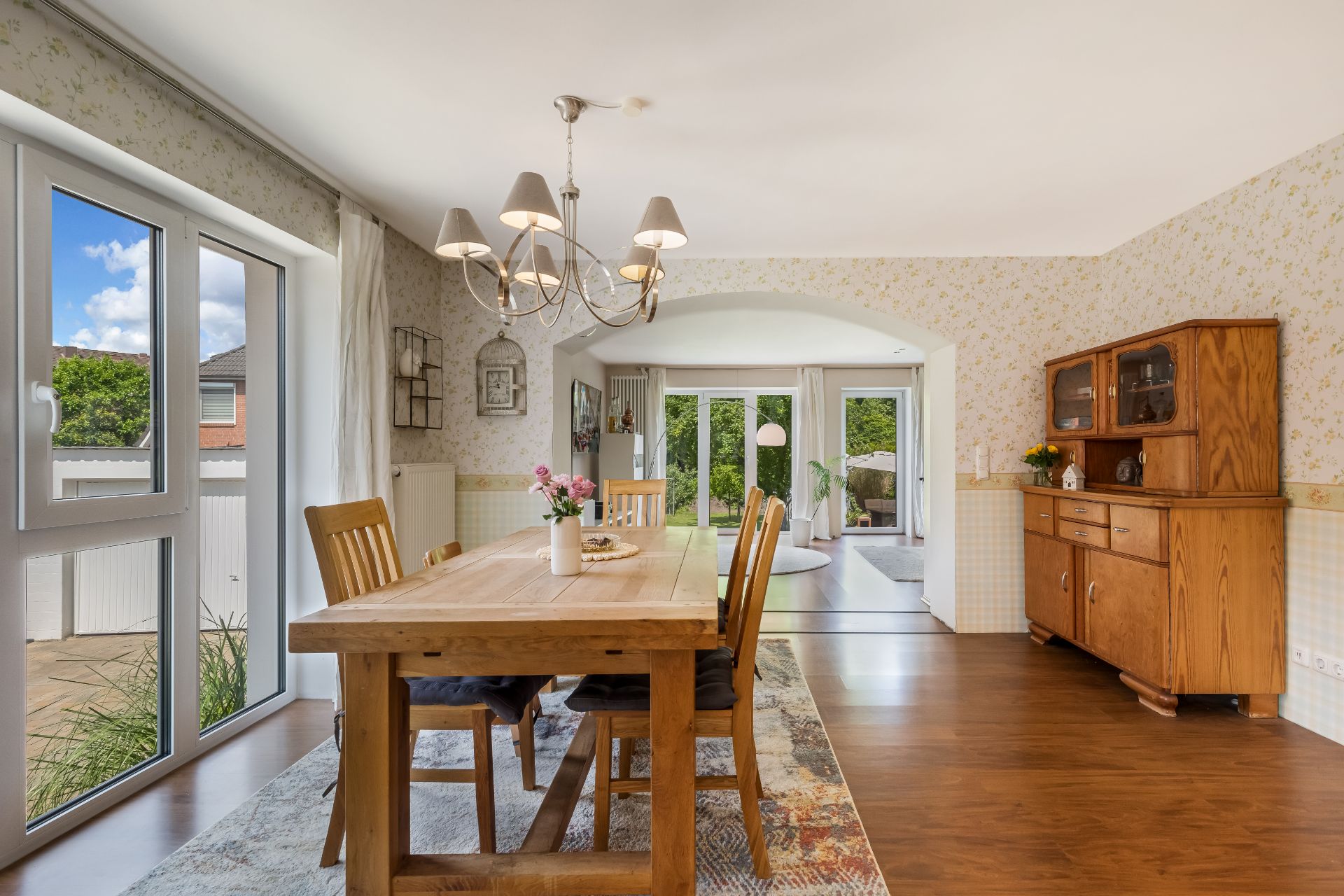 Esszimmer mit Holztisch, Stühlen und Vitrine, Blick in den Garten durch große Fenster.