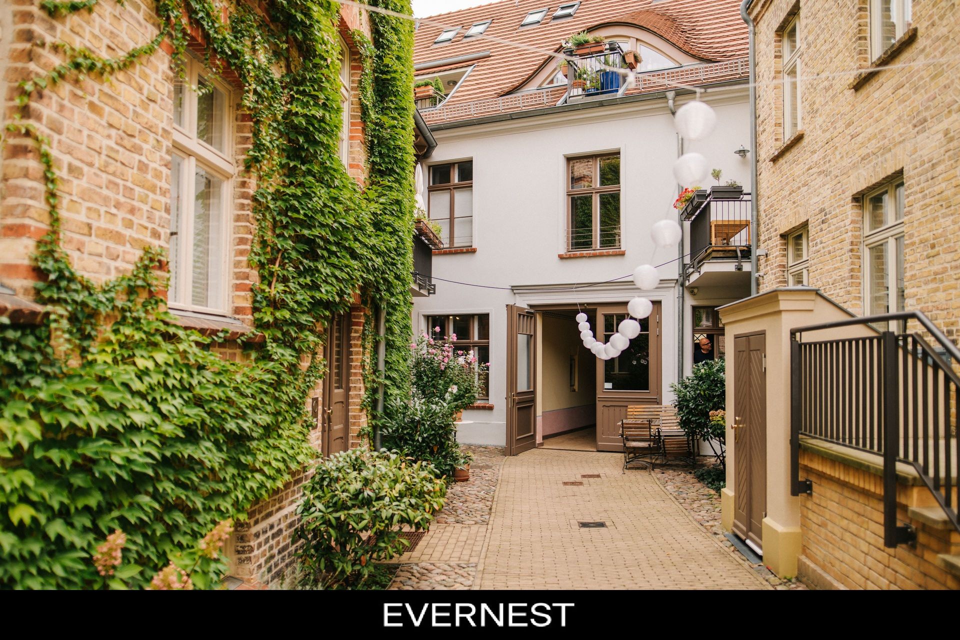 Gemütlicher Innenhof mit Pflanzen, Backsteinwänden und weißen Luftballons.