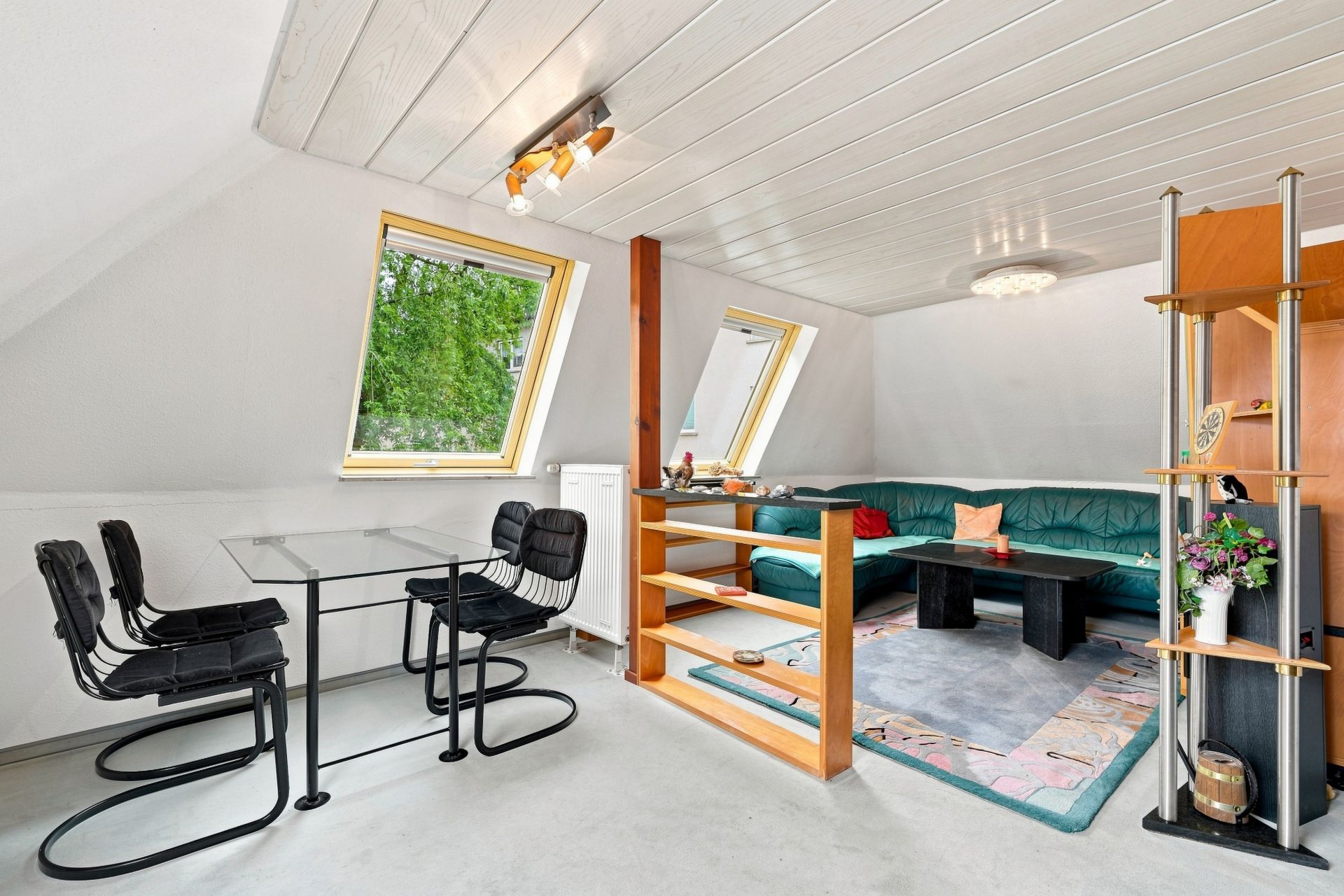 Helles Wohnzimmer mit grünem Sofa, Glastisch, schwarzen Stühlen und Dachfenstern.