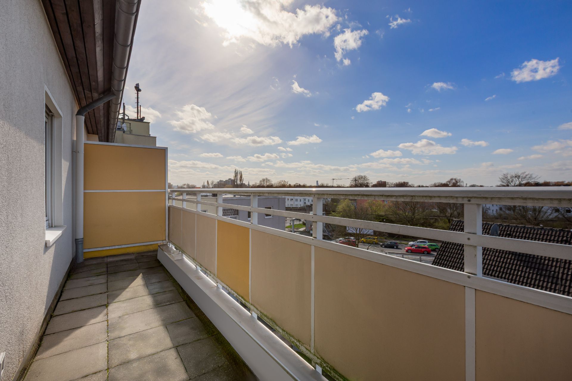 Balkon mit gelbem Sichtschutz und Blick auf Häuser und Bäume bei sonnigem Wetter.