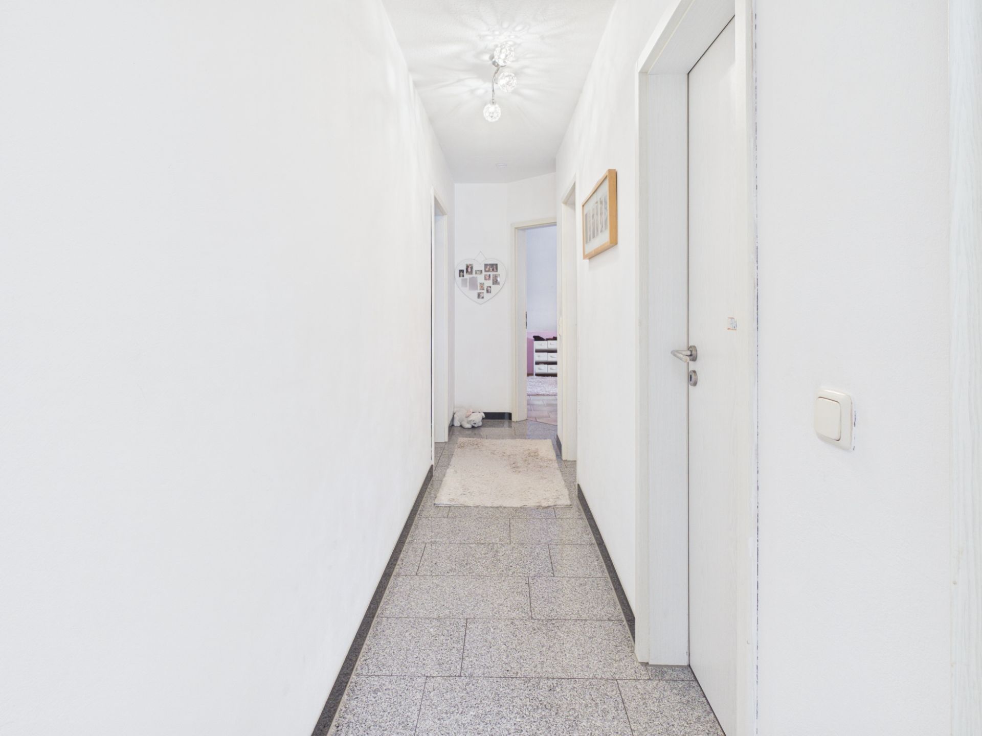 Heller Flur mit weißen Wänden, grauem Boden und mehreren Türen in einer Wohnung.