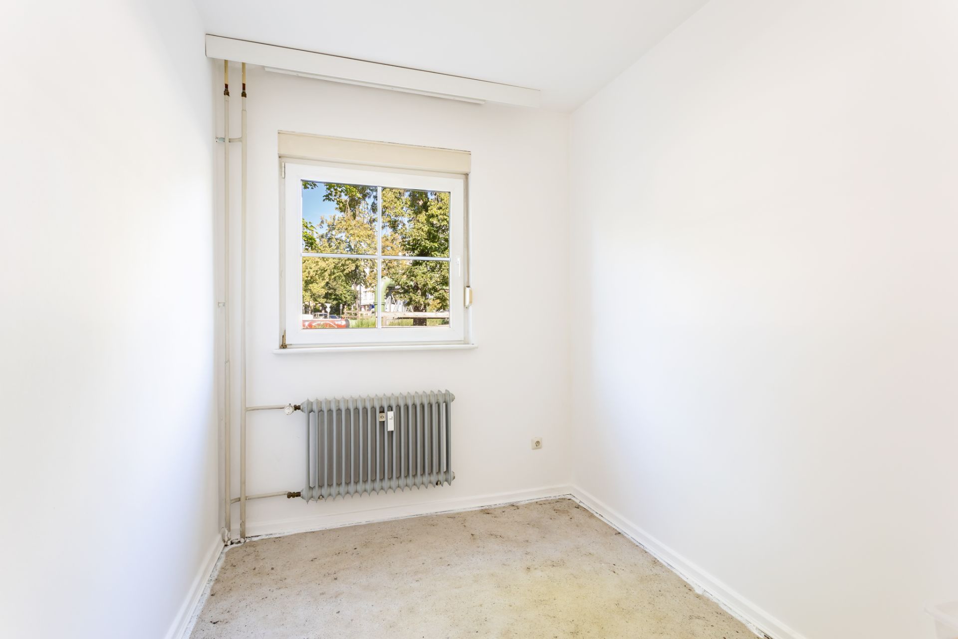 Kleines, leeres Zimmer mit weiß gestrichenen Wänden, Fenster und Heizkörper.