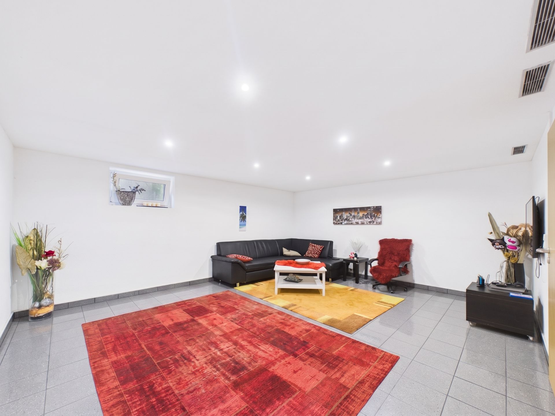 Helles Wohnzimmer mit Ecksofa, Couchtisch, rotem Teppich und Dekoration an den Wänden.