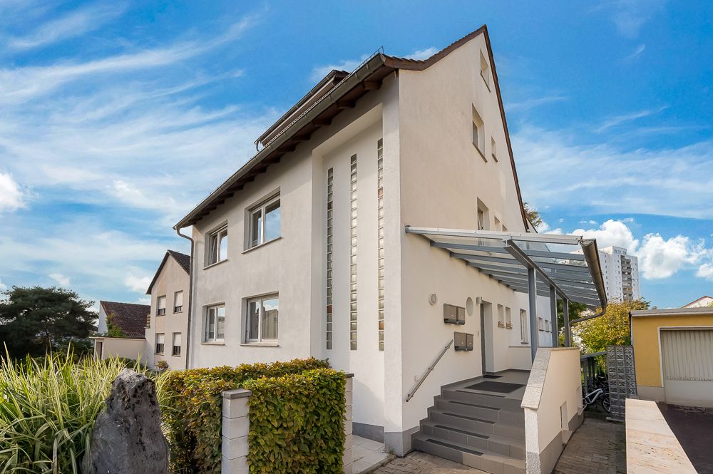 Modernes, weißes Wohnhaus mit Glasvordach und Treppe am Eingang, umgeben von Nachbarhäusern.