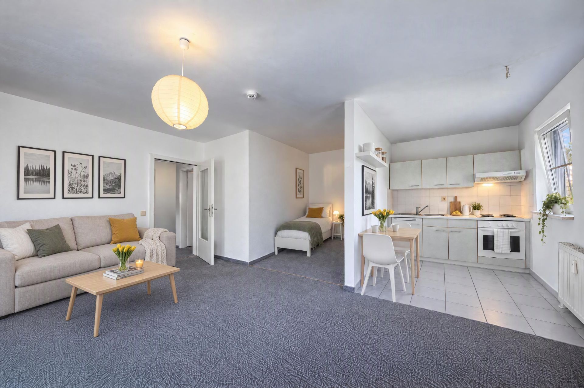 Helles Wohnstudio mit Sofa, Bett, Esstisch und offener Küche, dekoriert mit Bildern und Blumen.