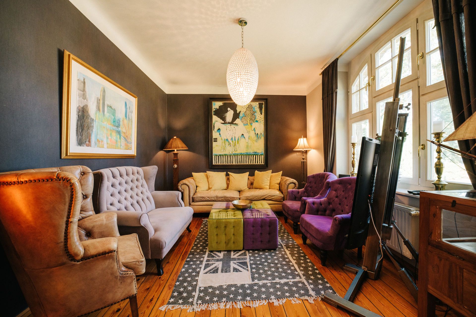 Wohnzimmer mit bunten Sesseln, Sofa, Teppich, Lampen und großer Fensterfront.