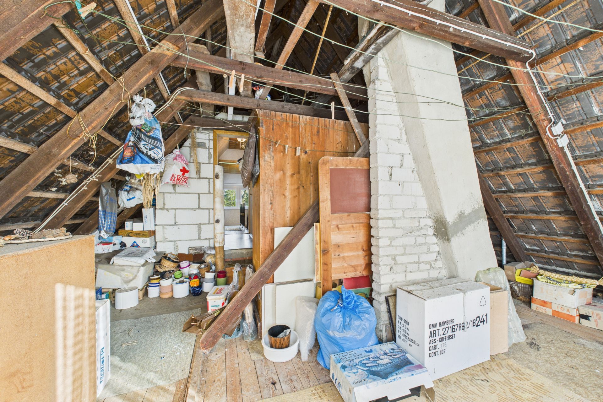 Unaufgeräumter Dachboden mit Holzgebälk, Kartons, Eimern und Baumaterialien.