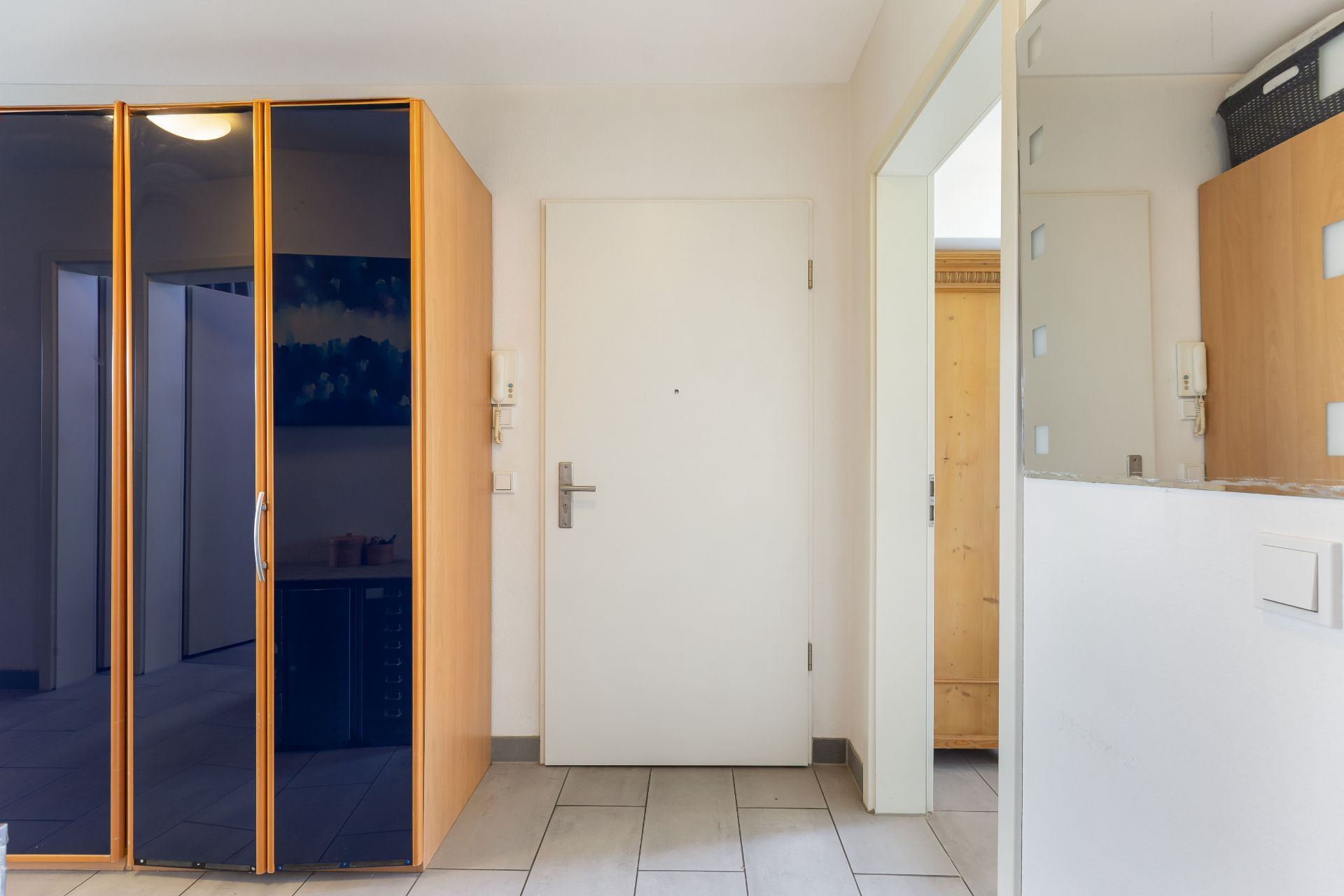 Eingangsbereich mit weißer Tür, großem Spiegelschrank und Fliesenboden.