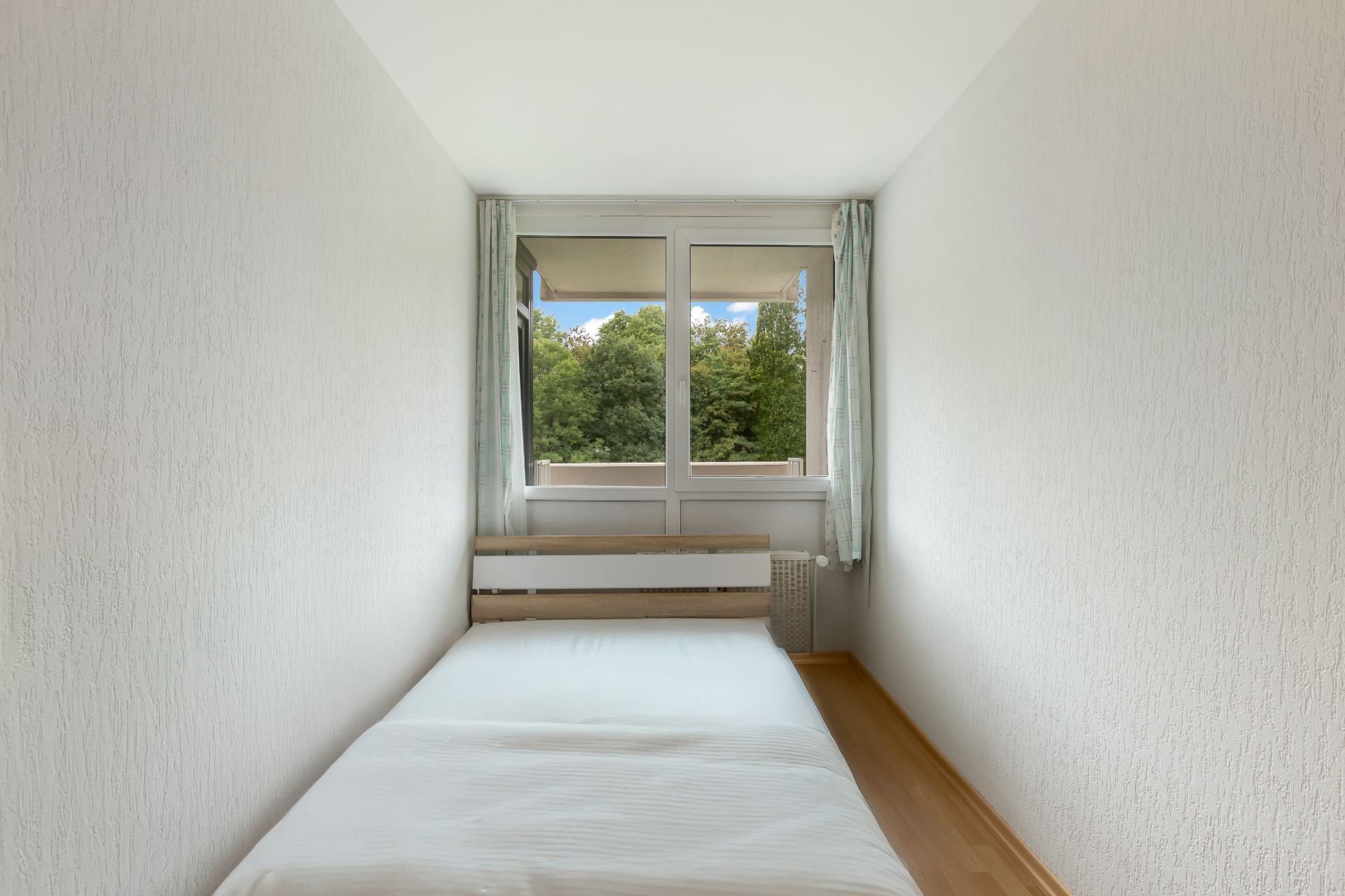 Schmales Schlafzimmer mit Einzelbett, Fenster und Blick ins Grüne.