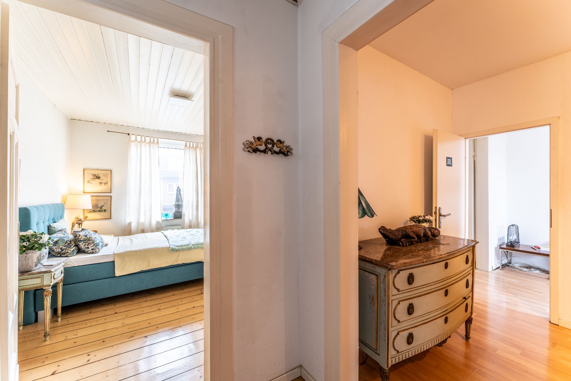 Heller Flur mit Blick ins Schlafzimmer und Nebenraum, Kommode im Vordergrund.