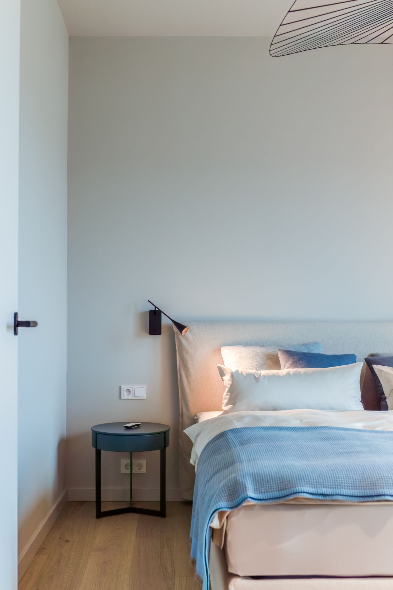 Modernes Schlafzimmer mit Bett, Nachttisch, Lampe und blauer Decke.