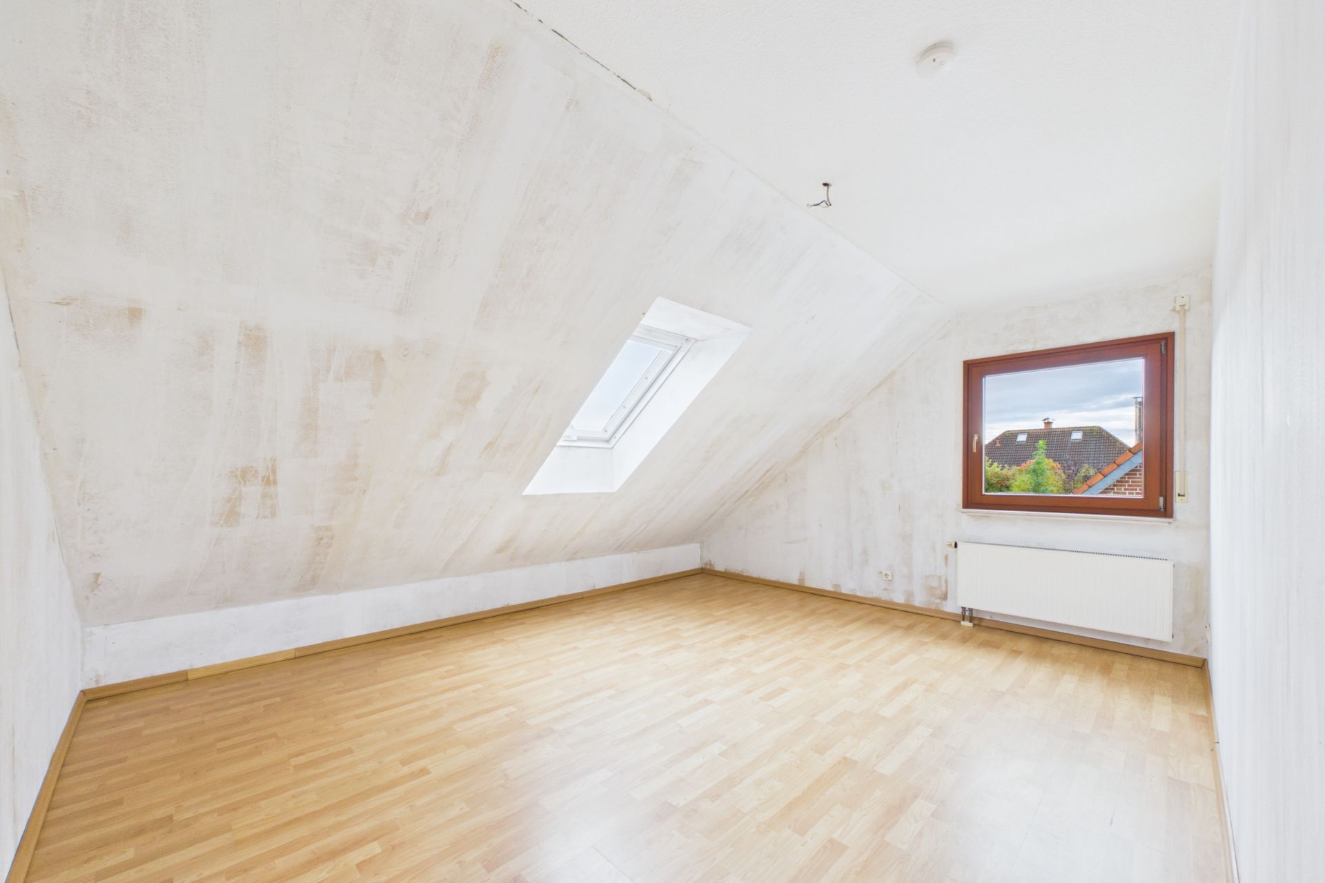 Heller Dachraum mit Schräge, Dachfenster, großem Fenster und hellem Laminatboden.