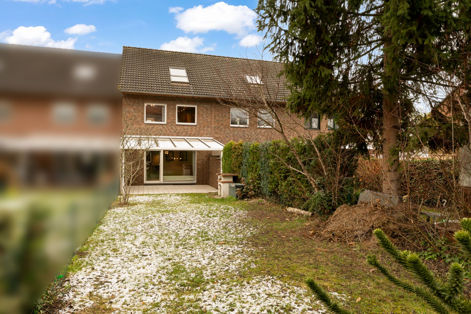 Rückansicht eines Backsteinhauses mit Garten, Terrasse und großen Fenstern.