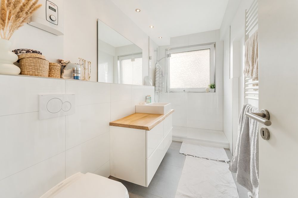 Modernes, weißes Badezimmer mit Waschbecken, Spiegel, Dusche und großen Fenstern.